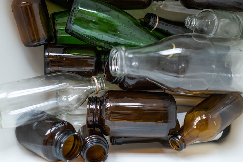 Three large black garbage bags filled with waste are positioned on a sidewalk near a fencing structure, with one bag leaning against the other two. The bags appear to be made of thick plastic and are